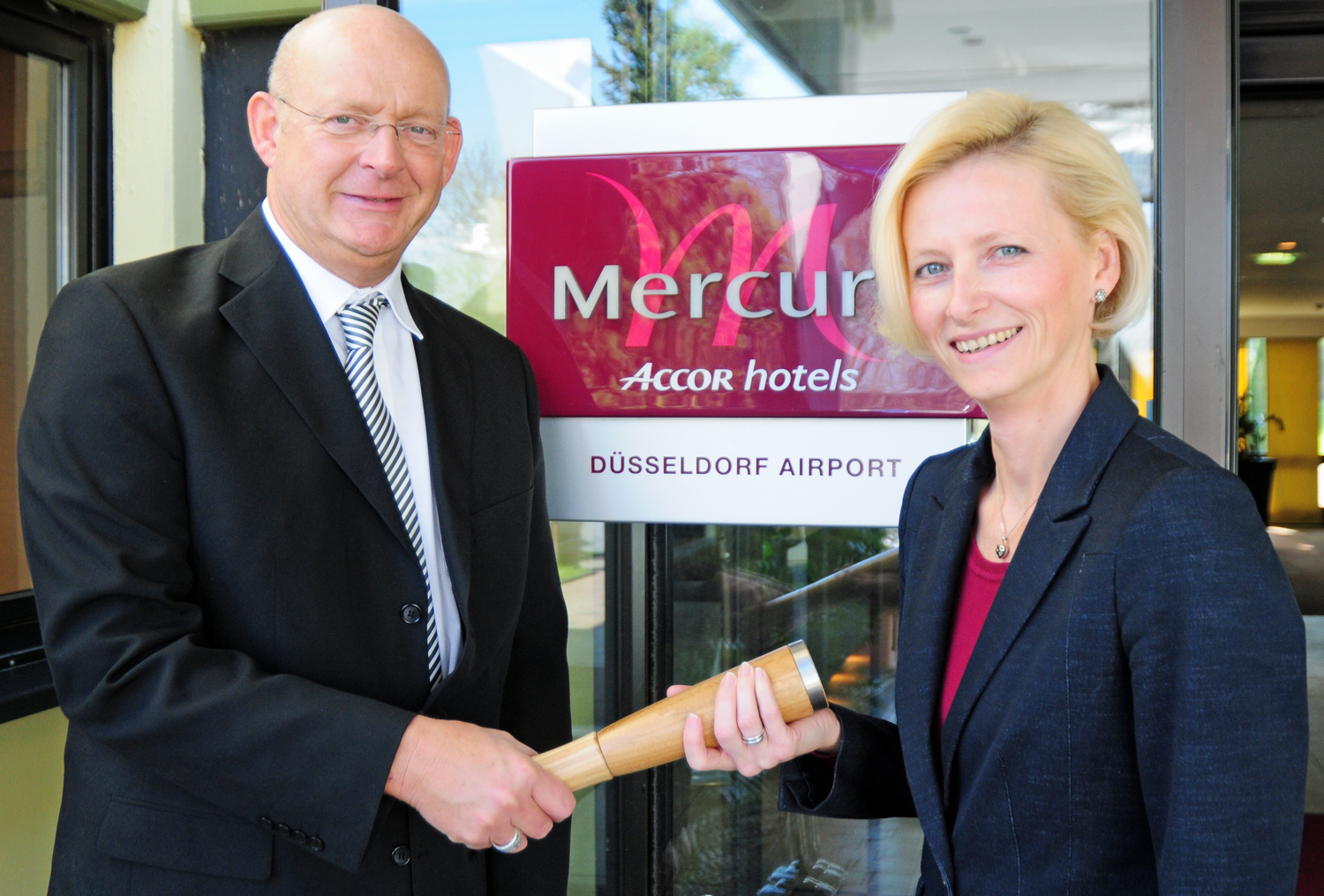 Der bisherige Direktor Jo Dahmen (l.) übergibt der neuen Direktorin Ludmila Zelena (r.) symbolisch mit dem Staffelstab die Verantwortung für das Mercure Hotel Düsseldorf Airport